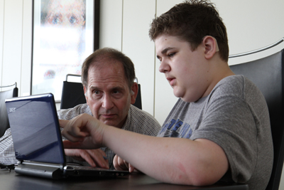 Photo of a student points to his computer in a discussion with a teacher