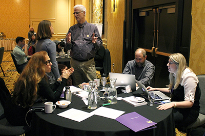 Two participants stand beside a table of three more, having multiple discussions.