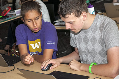 A student signs to another student while they work on a computer together. A student signs to another student while they work on a computer together.