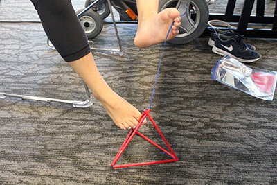 -	Phase I Scholar Teresa assembles a tetrahedron kite with her feet during Summer Study 2016.