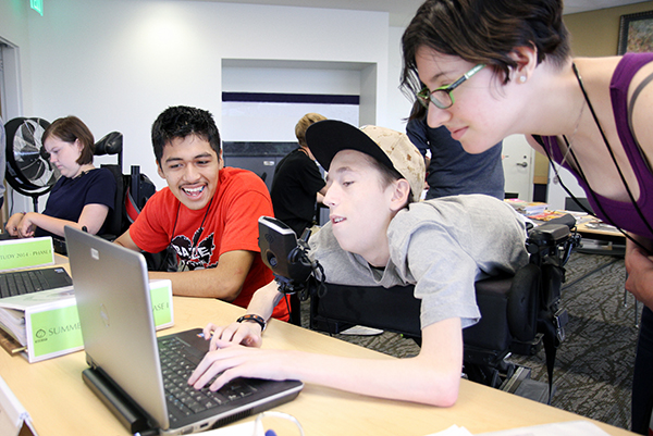 An intern helps two students complete a computing project.