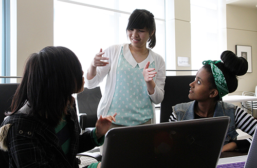 Three deaf students sign to each other in front of a computer.