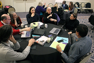 A large group of attendants discuss the conference presentations while sitting at a table.