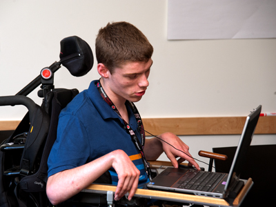 Photo of DO-IT Scholar Cody Hinkley using a laptop computer in his wheelchair