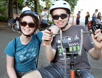Eric sits on an accessible bike while Hannah sits next to him, both smiling at the camera.