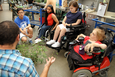 Four students sit around an instructor with a large plant in the UW greenhouse.