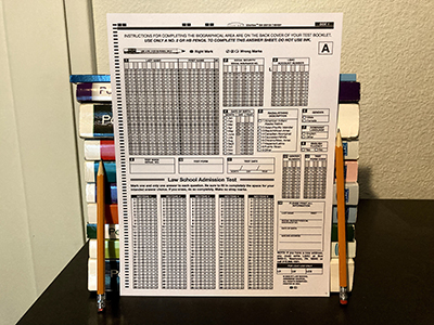 An LSAT bubble answer sheet propped against a stack of books, with a pencil on either side.