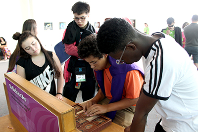 Four students gather around an activity on a table, with one student working on the activity.
