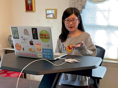 A computing student talks to someone over the computer at a standing desk.