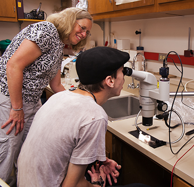 A participant examines a biology specimen through a microscope while a mentor watches.