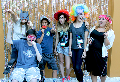 One DO-IT Staff member and five Scholars pose in silly ways wearing silly hats and masks in front of a sparkly background