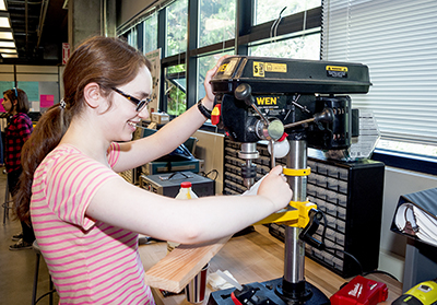 DO-IT Intern Hannah puts a piece of wood into a machine in the UW CoMotion Makerspace.