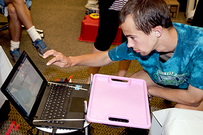 Phase Two Scholar Jason touches a laptop attached to a machine, which is Chester, the Turtlebot.