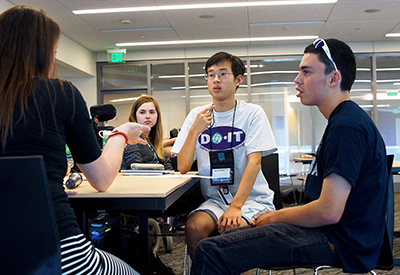 Phase II Scholar Sangha gestures while answering a question. DO-IT Staff Tami and DO-IT Interns Antonio and Jessica also sit at the table.