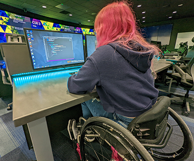 A student in a wheelchair codes on a computer. A student in a wheelchair codes on a computer.