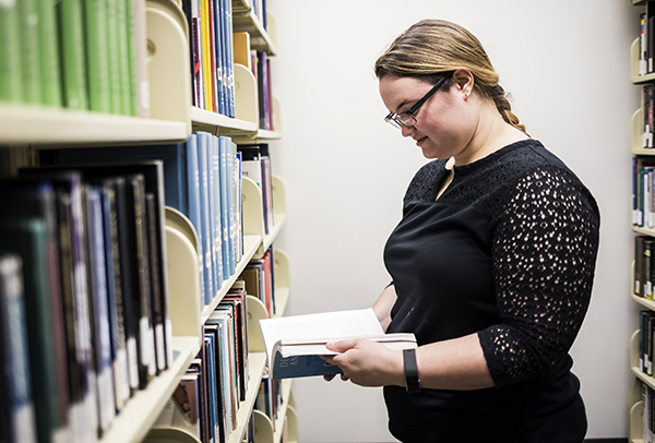 A student looks at a book next to a bookshelf in the library.