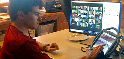 A student uses an assistive communication device to talk while on Zoom.