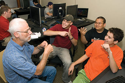 Richard signs with a group of students surrounded by computers.