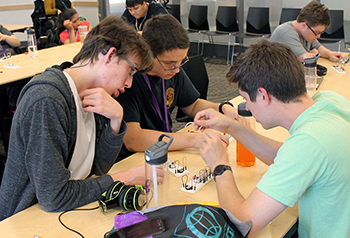 A mentor shows two students how to assemble circuitry for a keyboard.