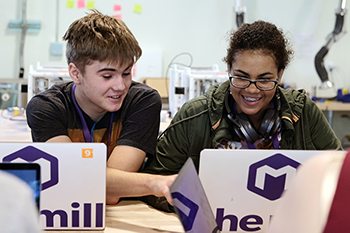 Two students laugh while using a computer.