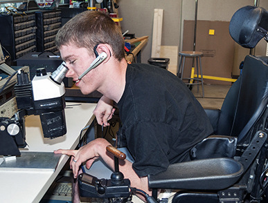 A student in a wheelchair looks into a microscope.