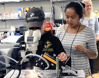 A student and a teacher looking into a microscope.