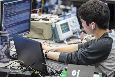 A student codes while surrounded by multiple computers.