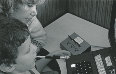 Sheryl works with Rodney to use an assistive switchbox and mouth rod.