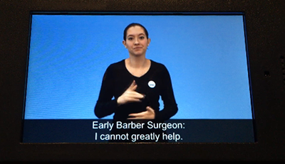 Video still of an audio tour that has a sign language interpreter as well as closed captions.