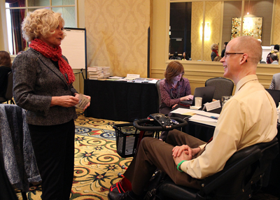 Photo of DO-IT Director Sheryl Burgstahler talks with AccessSTEM CBI Participant Christopher Andersen in the lecture room at the Hotel Deca in Seattle.