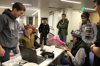 Photo of a group of DO-IT participants chat amongst themselves and with CSNE staff while looking at a laptop.