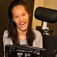 A student with a communication device and wheelchair smiles at the camera.