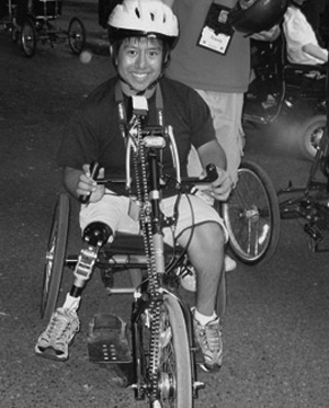 Photo of DO-IT Scholar smiles while riding a modified bicycle with hand peddles