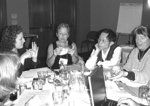 Photo of discussion between participants at a round table is aided by a sign language interpreter and laptop computer