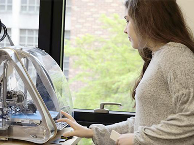 Video still showing a woman looking at a 3D printer