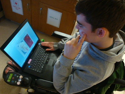 Photo of a male student in a wheel chair working on a laptop