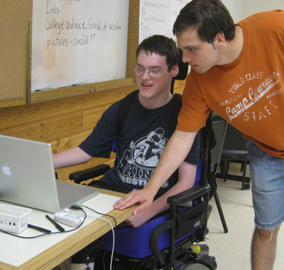 Picture of a Courage Camper in a wheelchair working on a laptop while the instructor observes.