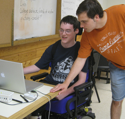 Picture of a Courage Camper in a wheelchair working on a laptop while the instructor observes.