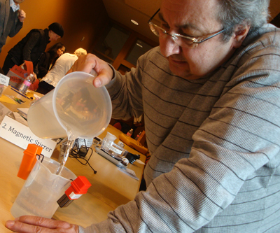 Photo of Al Souma pours water into a container that has a device attached to it that will beep when the water gets to a certain level.