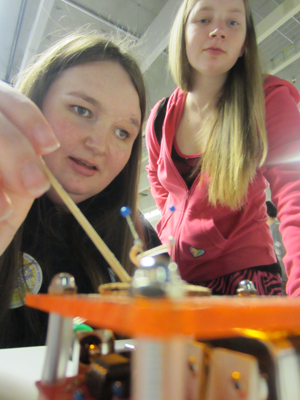 Photo of two female students use electrodes to conduct an experiment.