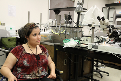 Photo of 2011 Scholar Deicy sits next to a microscope, lab sink, and other various lab equipment.