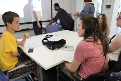 Photo of 2012 Scholar Nolan working with 2010 Intern Marlise, papers, a calculator, a backpack, and an iPad between them.