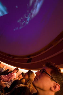 Photo of people sitting around the edge of the University of Washington planetarium looking up at the night sky on a giant screen