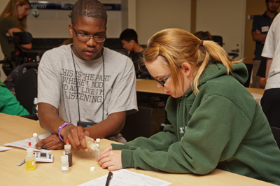 Photo of Phase I DO-IT Scholars Julian and Karly holding different bottles of chemicals and work together in a classroom.