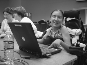 Photo of DO-IT Scholar in wheelchair smiling at the camera while she uses the touch-pad on her laptop.