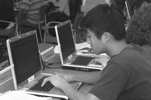 Image of a DO-IT Scholar typing on one of many laptops on a table.