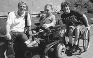 DO-IT Scholars with staff member Scott. Two DO-IT Scholars in wheelchairs pose for a picture with Staff member Scott