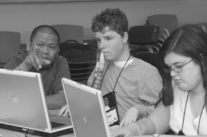 Image of three Scholars gather around two laptops, brainstorming.