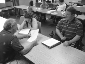 Photo of two students are interviewed by an adult and interviews are going on in the background.