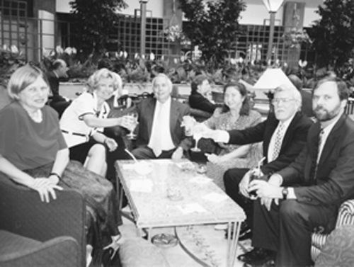 Photo of Six adults sit around a table and raise their glasses for a celebration toast.